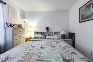 Ett sovrum med en säng, byrå, sängbord, lampor och tavlor på väggen.