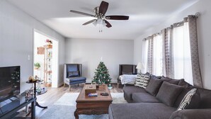 Una sala de estar con sofá, televisor, mesa de centro y ventilador de techo.