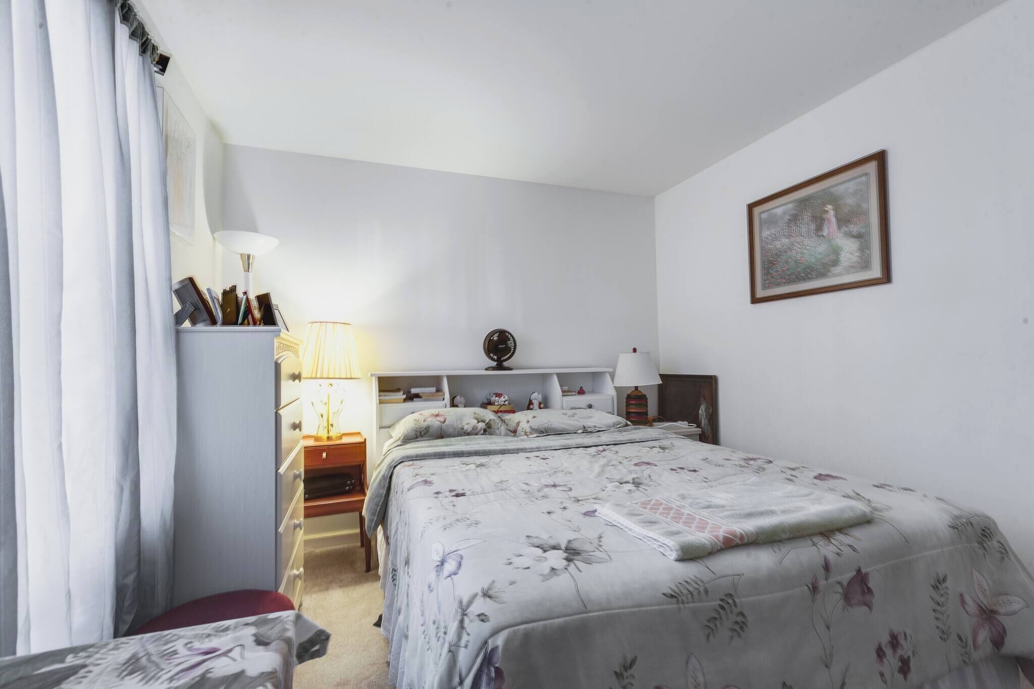 Une chambre à coucher avec un lit, des tables de chevet, une lampe, une commode et un tableau au mur.