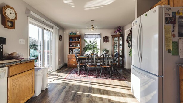 Una cocina con comedor, armarios de madera, un refrigerador y un reloj en la pared.