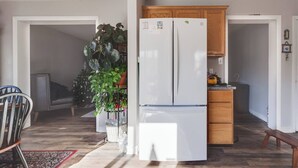 Una cocina con refrigerador blanco, armarios de madera y un comedor con una silla y una mesa.