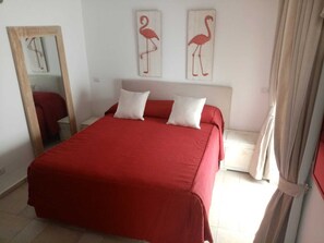 A room with a bed, two pillows, a mirror, and two wall-mounted artworks of flamingos.