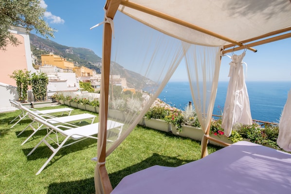 Unwind in a serene outdoor setting with a clear view of the sea, featuring a well-maintained lawn and comfortable lounge chairs under a shaded canopy.