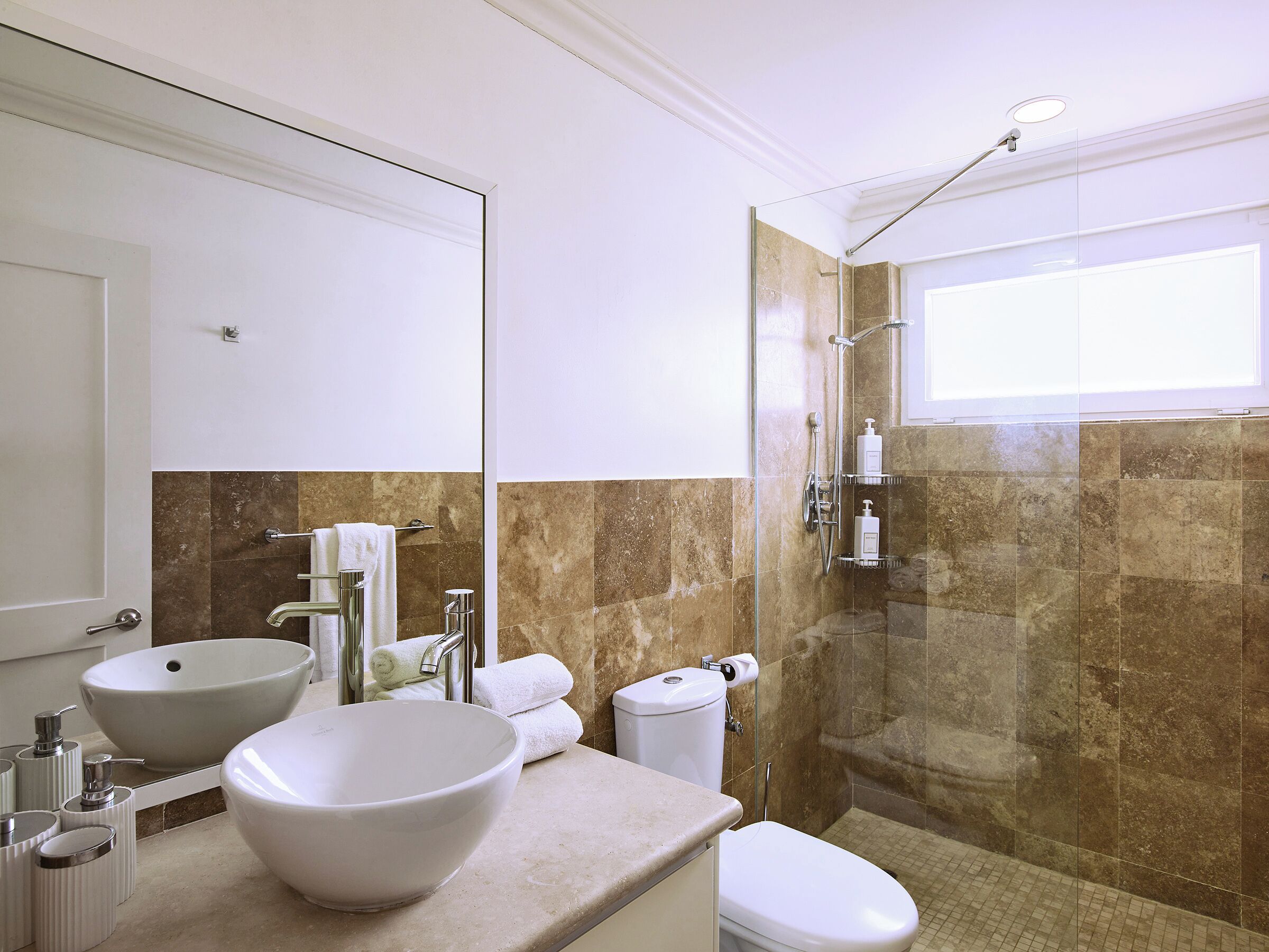 Une salle de bain avec un grand lavabo blanc, des toilettes, une douche à parois de verre et un miroir au-dessus du lavabo.