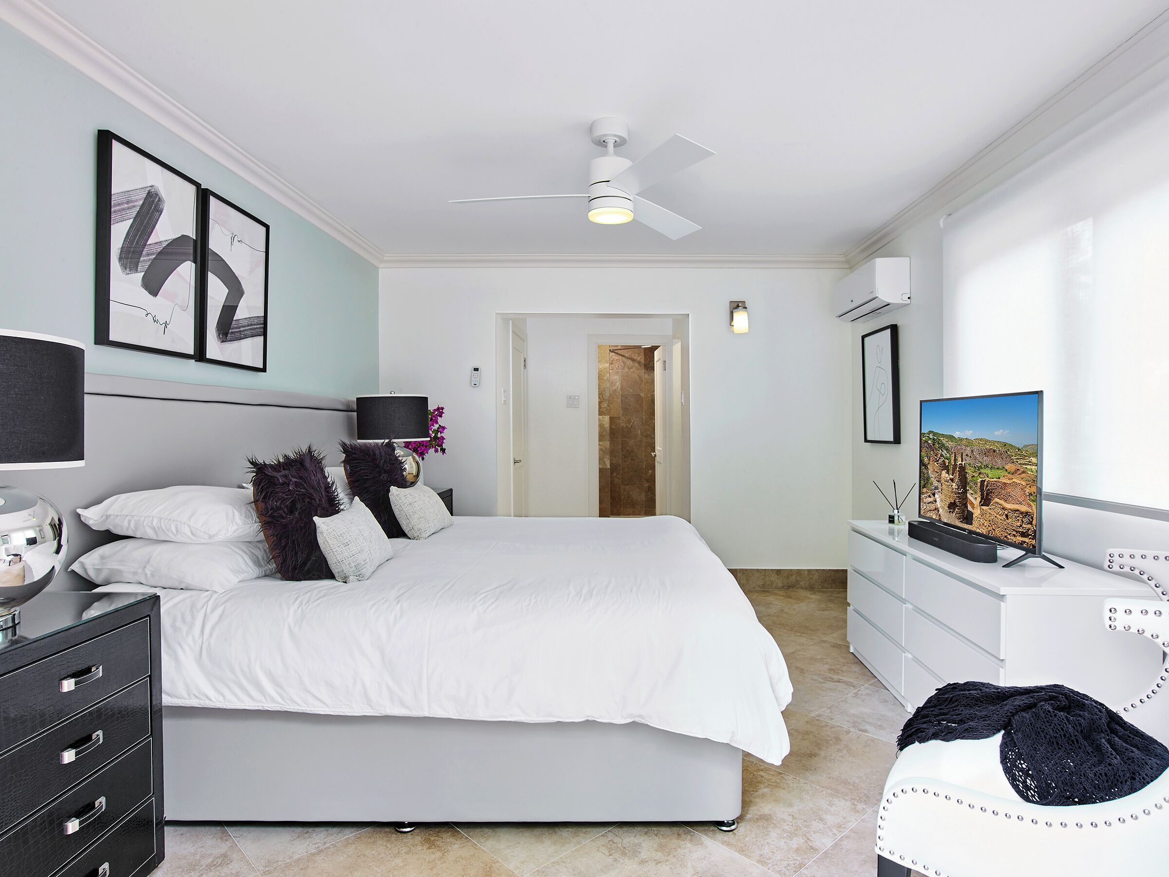 Ein modernes Schlafzimmer mit Bett, Nachttisch, Lampe und Fernseher.