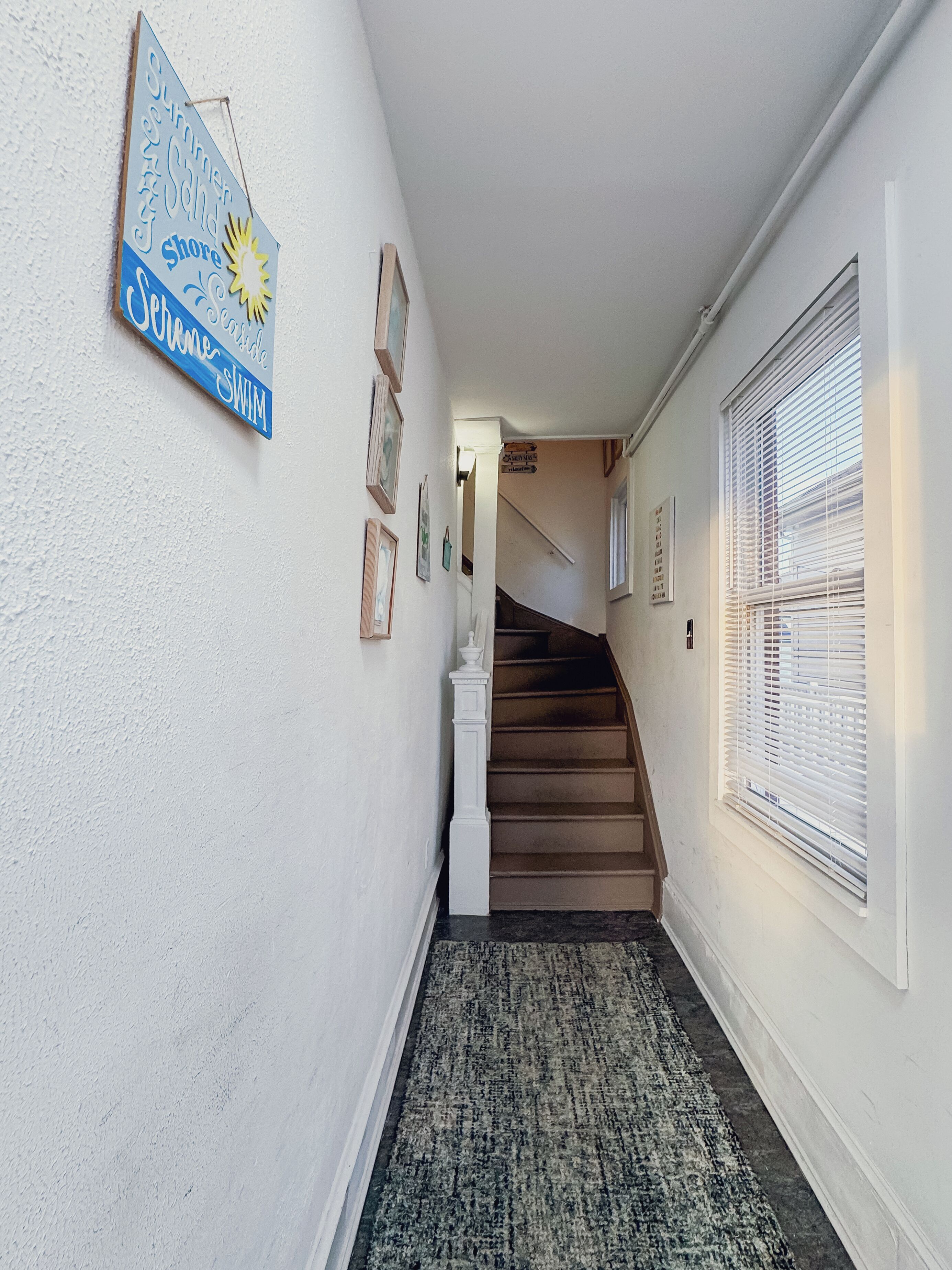 Un couloir avec un escalier, un tapis et un panneau sur le mur.