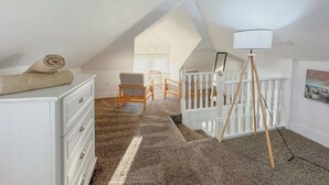 A spacious attic bedroom with a sloped ceiling, a white dresser, a rolled-up towel, a wooden chair, a small table, a white railing, and a floor lamp. - Wildwood Private ✳ 3BR 2BA APT ✳ 5 min walk to Beach & Boardwalk ★★★★★ Location! (Wildwood)