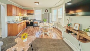 A modern kitchen with wooden cabinets, a dining area with a wooden table and chairs, and a large window providing natural light. - Wildwood Private ✳ 3BR 2BA APT ✳ 5 min walk to Beach & Boardwalk ★★★★★ Location! (Wildwood)