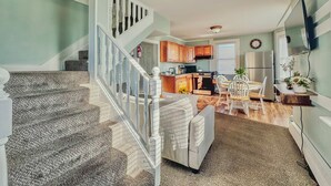 A spacious living area with a staircase, a dining table with chairs, a kitchen with modern appliances, and a large window providing natural light. - Wildwood Private ✳ 3BR 2BA APT ✳ 5 min walk to Beach & Boardwalk ★★★★★ Location! (Wildwood)