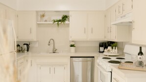 Una cucina moderna con mobili bianchi, lavastoviglie, piano cottura e lavello.