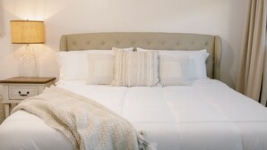 Un letto ben rifatto con una testiera imbottita, una lampada da comodino e un piccolo tavolino con un cassetto.