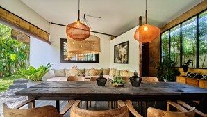 A wooden dining table with chairs, a sofa with cushions, and hanging woven light fixtures. - Tropical Designer Private Villa, 3br, Umalas (Kerobokan)