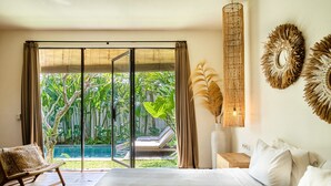 A bedroom with a large bed, a chair, and a view of a swimming pool and lush greenery. - Tropical Designer Private Villa, 3br, Umalas (Kerobokan)