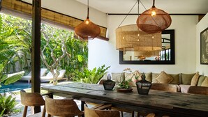 A wooden dining table with chairs, surrounded by lush greenery and a pool. - Tropical Designer Private Villa, 3br, Umalas (Kerobokan)