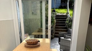 A dining area with a wooden table and benches, a glass door leading to a garden, and a tiled floor. - Castle Cottage in Conwy - 2 minute walk into Conwy yet has delightful garden (Conwy)