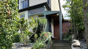 A two-story house with a stone staircase leading to the front door, surrounded by greenery and a wooden fence. - Castle Cottage in Conwy - 2 minute walk into Conwy yet has delightful garden (Conwy)
