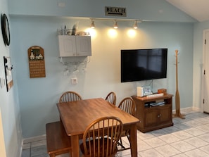 A dining area with a wooden table and chairs, a TV mounted on the wall, and a sign indicating 'BEACH'.