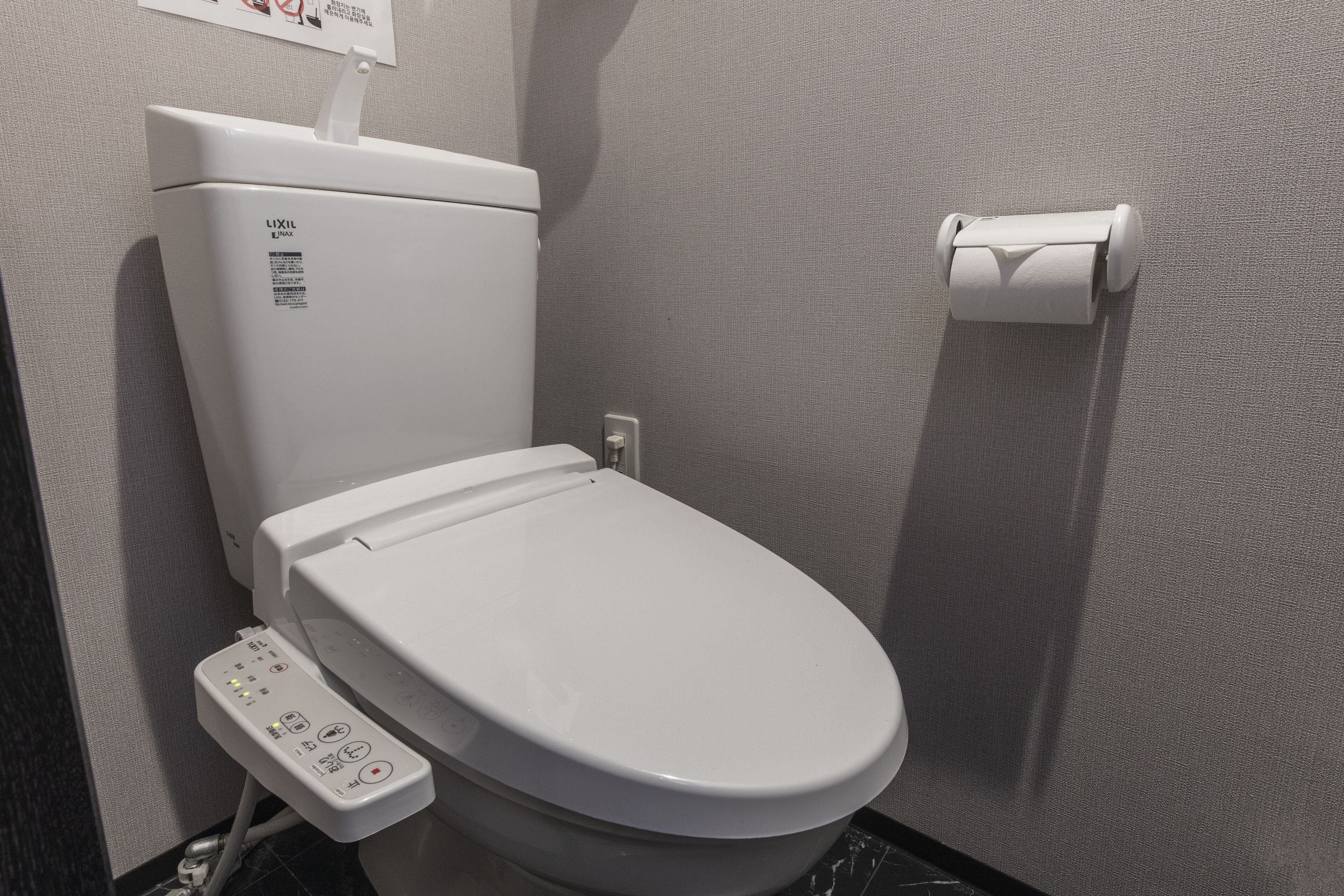 A modern toilet with a control panel, a toilet paper holder, and a wall-mounted sign.