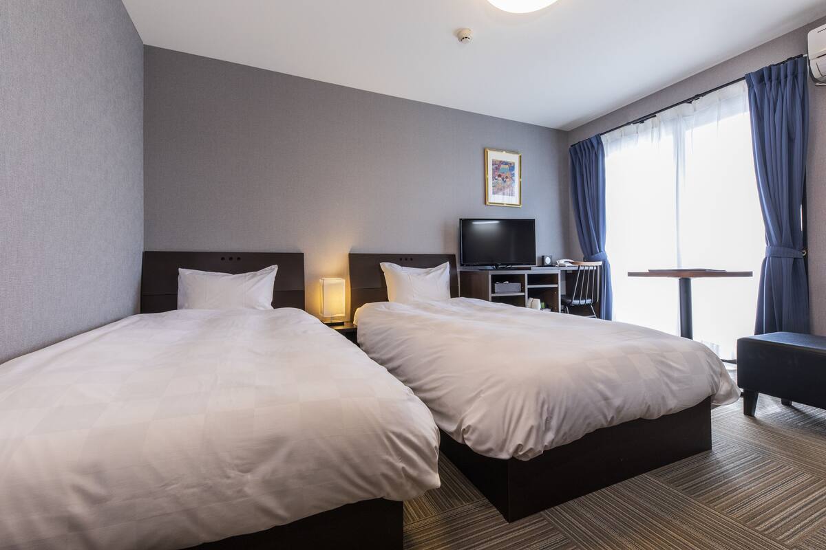 A hotel room with two beds, a TV, a desk, and a chair.