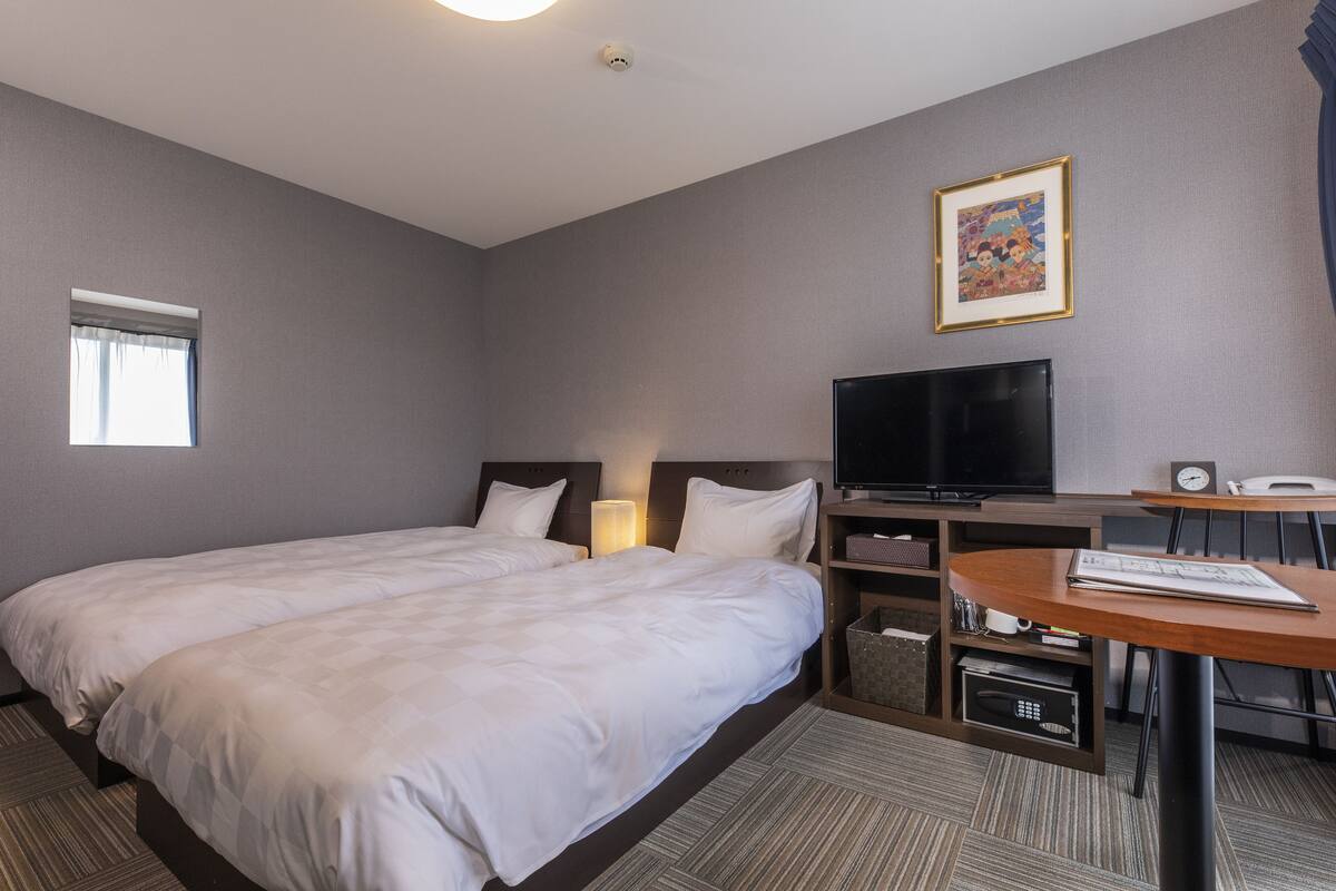 A hotel room with a large bed, a desk with a chair, a television, and a small table with a keyboard.
