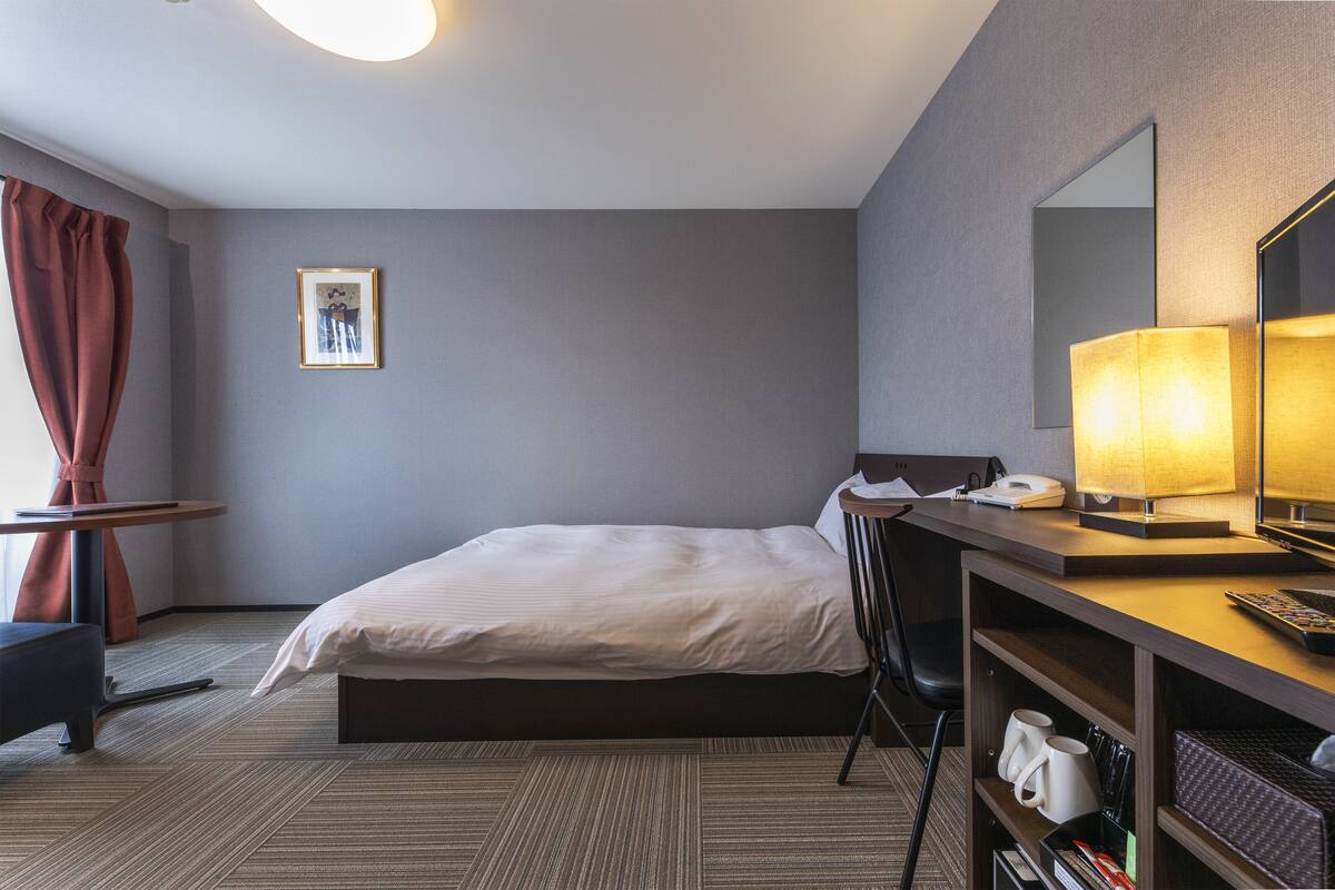 A hotel room with a bed, desk, chair, and a large mirror.