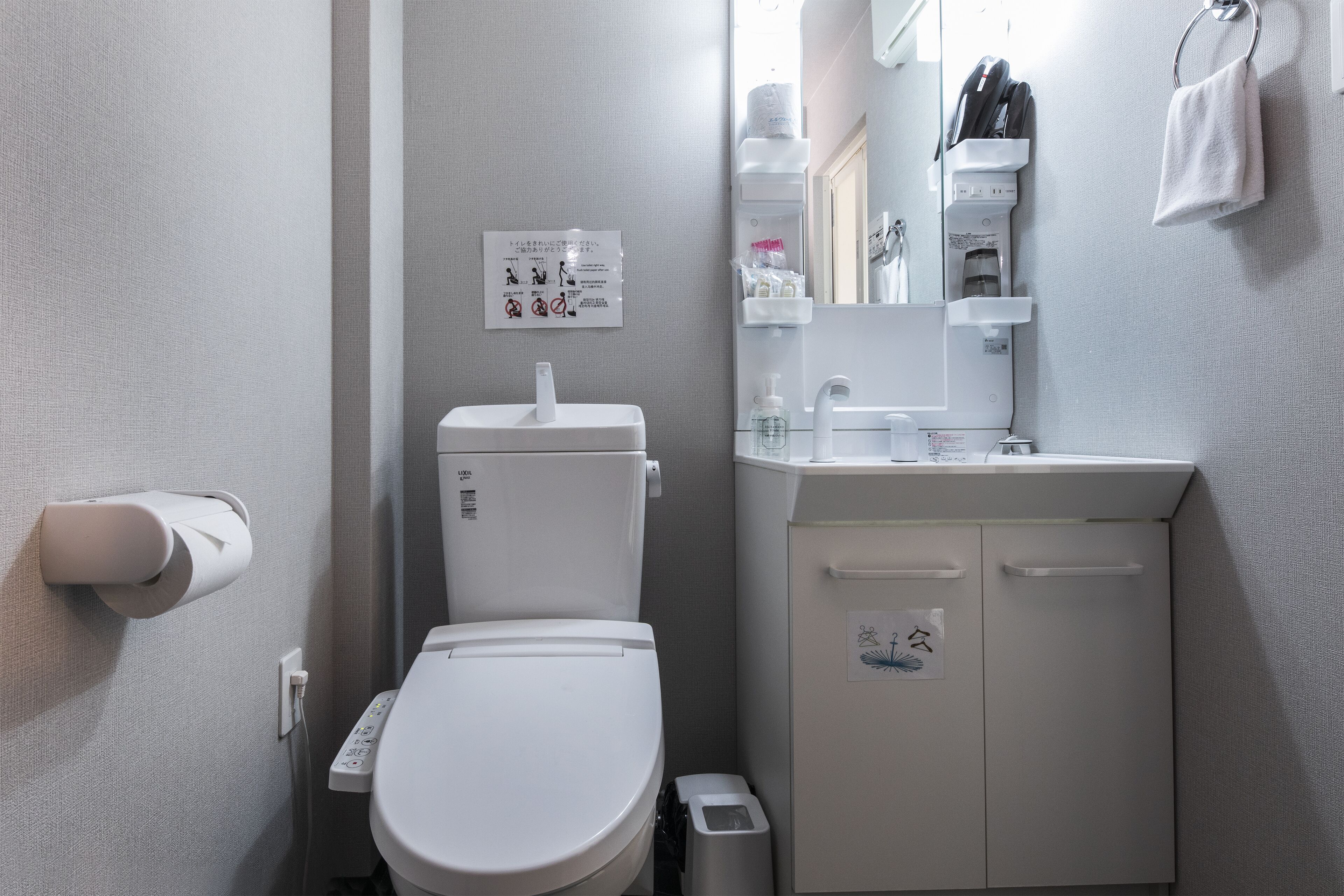 Une salle de bain moderne équipée de toilettes, d’un lavabo et d’un sèche-mains. Un panneau avec des instructions est affiché sur le mur.