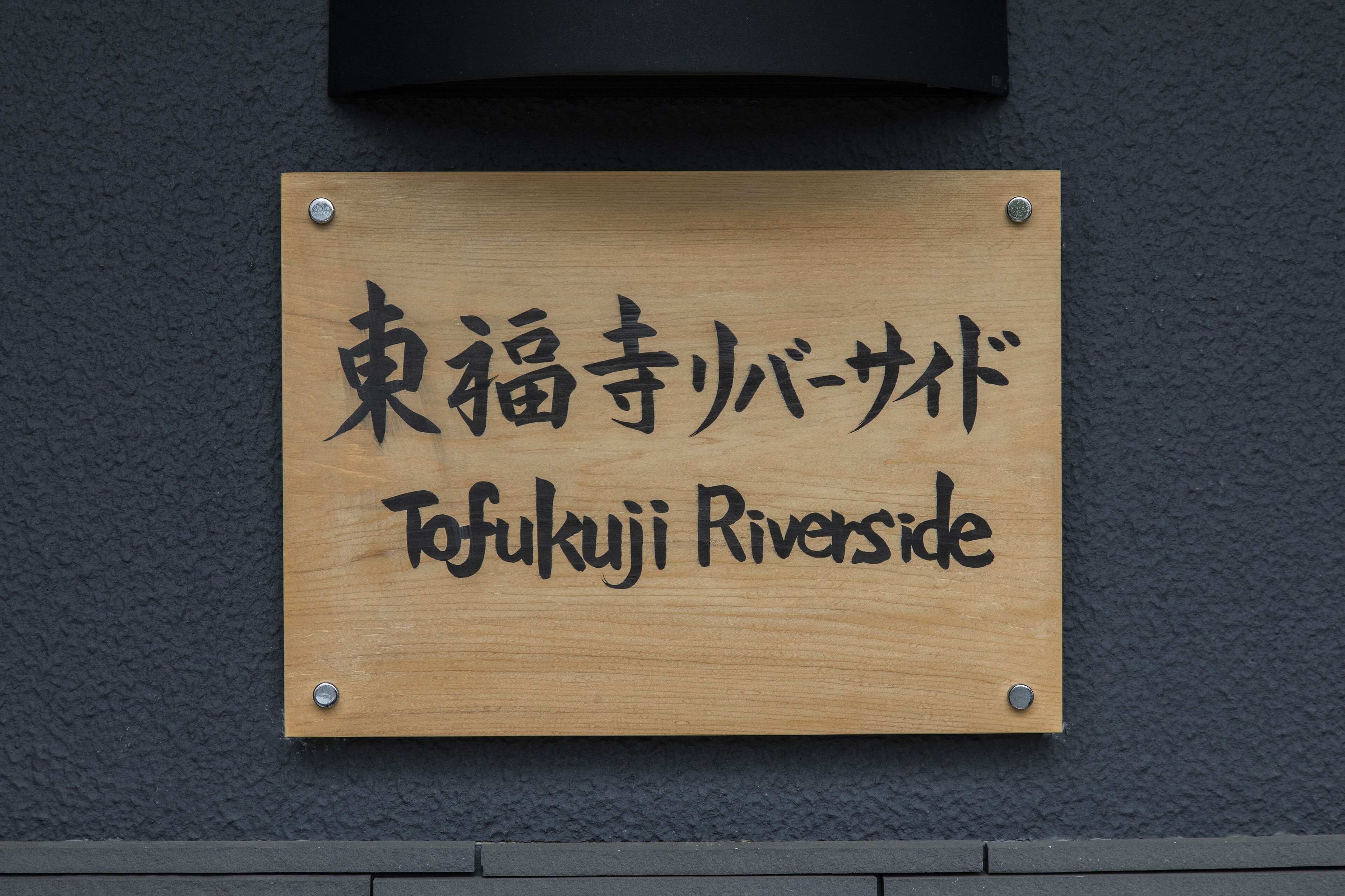 A wooden sign with Japanese characters and the English translation "Tofukuji Riverside".