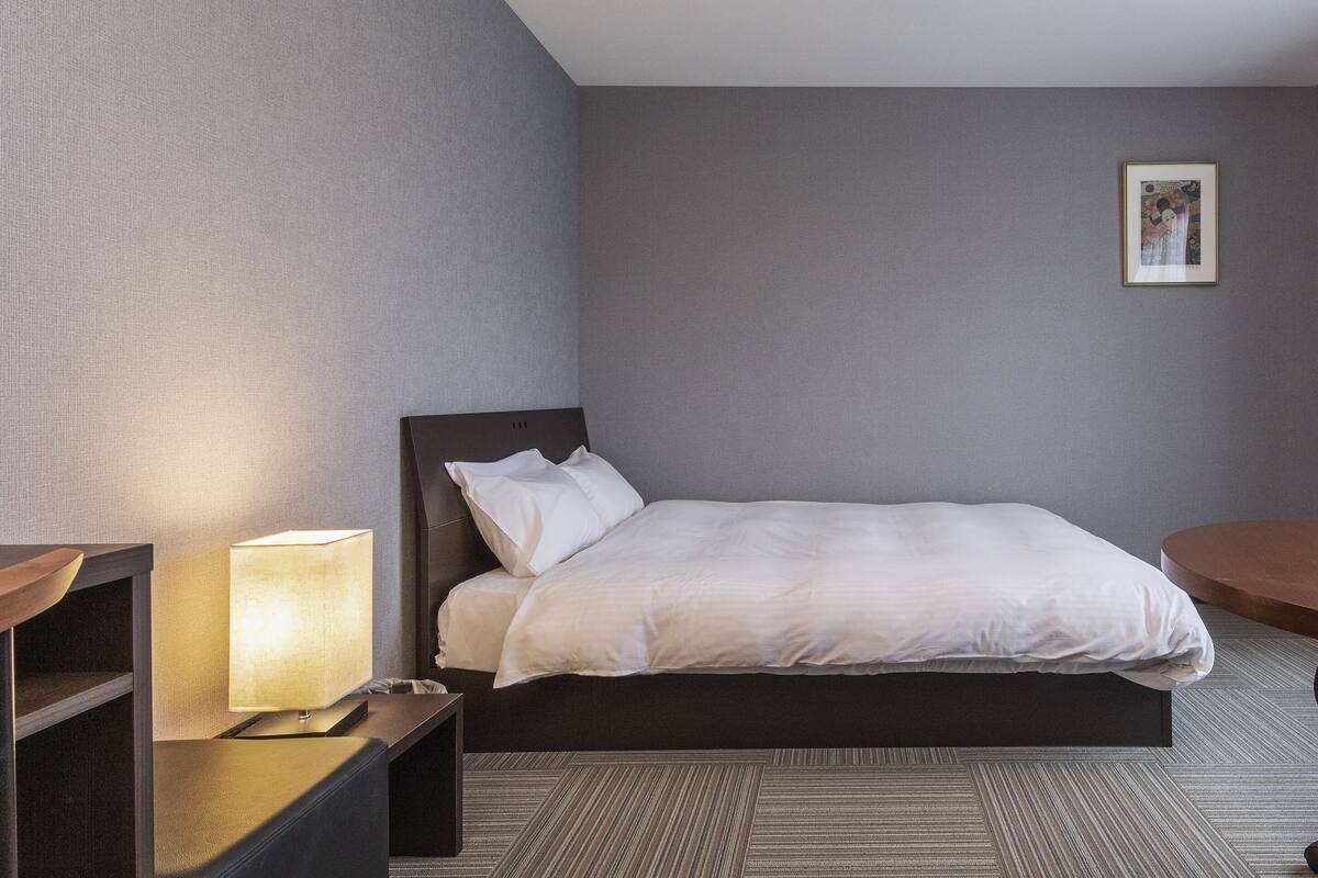 A hotel room with a bed, bedside table, lamp, and a framed picture on the wall.