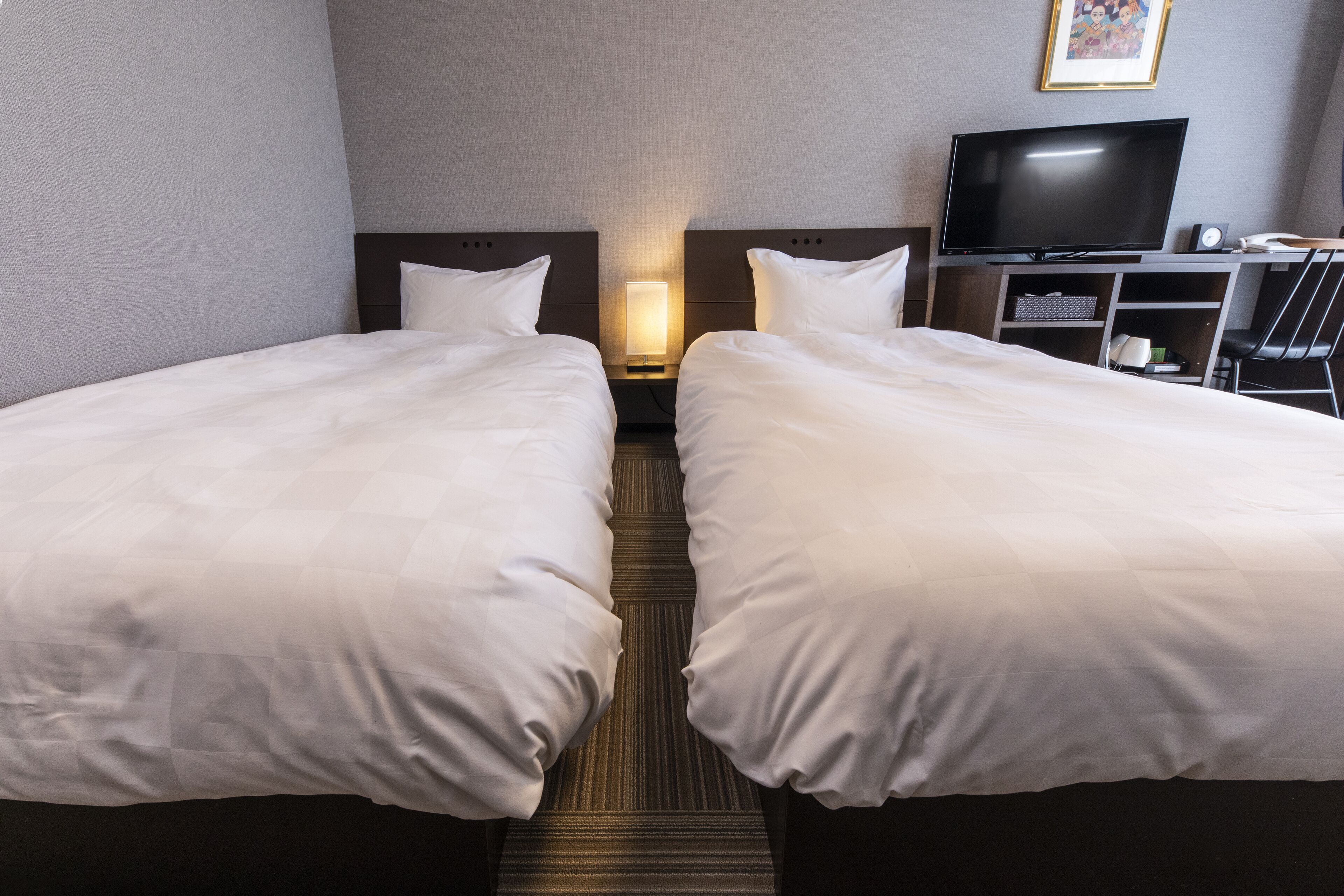 Ein Hotelzimmer mit zwei Betten, einem Fernseher und einem Schreibtisch mit Stuhl.