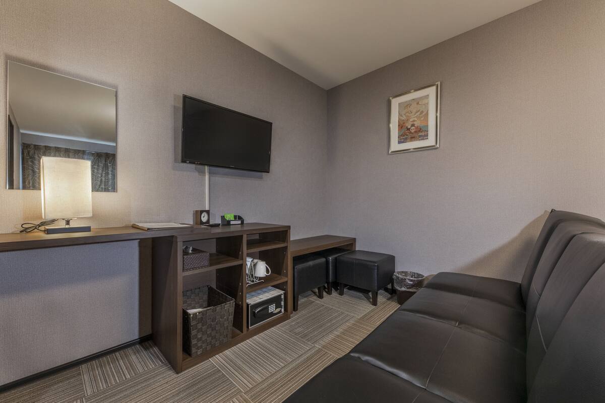 A modern hotel room with a flat-screen TV, a desk with a lamp, a sofa, and a small coffee table.