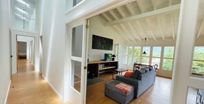 A spacious living area with a large window, a sofa, a TV, and a wooden desk.