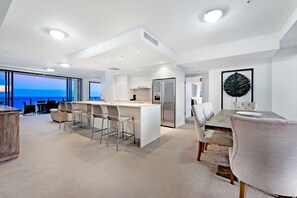 A modern kitchen with a central island, bar stools, and a dining area with a large table and chairs.