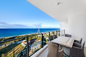 A balcony with a table and chairs, overlooking a beach and a construction site with a crane.