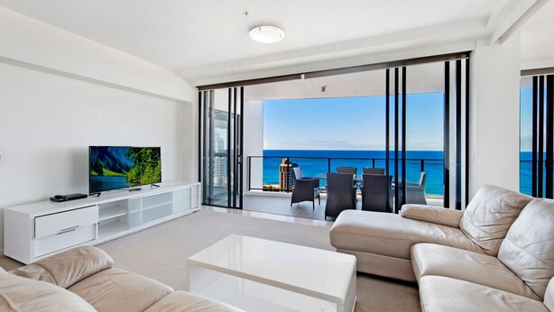 Sala de estar moderna com televisão, sofá e varanda com vista para o mar.