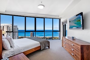 Une chambre avec une grande fenêtre, un lit, une commode et un téléviseur à écran plat.