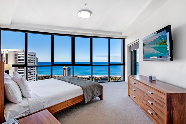 A bedroom with a large window, a bed, a dresser, and a flat-screen TV.