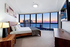 Ein Schlafzimmer mit einem großen Bett, einem Schreibtisch und Blick auf das Meer und Gebäude.
