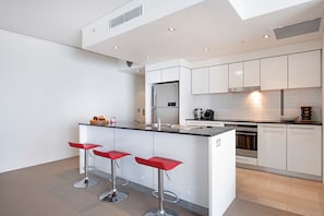 Une cuisine moderne avec des meubles blancs, un îlot central doté de tabourets et des appareils électroménagers intégrés.