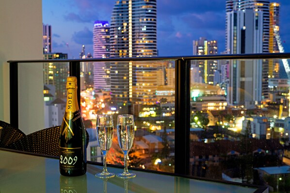 Une bouteille de champagne et deux verres sur une table, avec une vue sur la ville à travers une fenêtre.