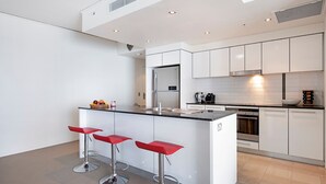 Una cocina moderna con armarios blancos, una encimera negra y tres taburetes rojos.