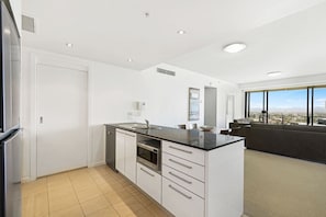 Een moderne keuken met witte kasten, een zwart aanrecht en stadszicht door grote ramen.
