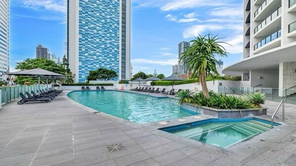 A rooftop swimming pool with lounge chairs, surrounded by modern buildings and greenery.