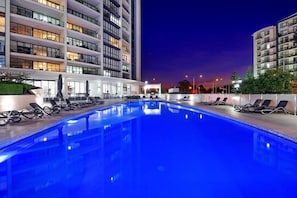 A swimming pool with lounge chairs, surrounded by modern buildings with balconies. - Hinterland Views 2BR apartment - Sierra Grand (Broadbeach)