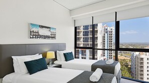 Two single beds with white linens and dark green pillows, a grey headboard, and a bedside table with a lamp.