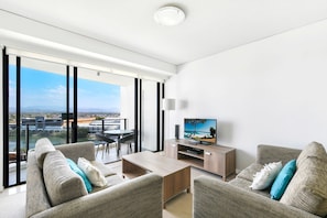 A modern living room with a balcony, a flat-screen TV, and a dining area with a table and chairs.