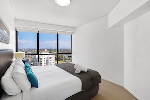 Een hotelkamer met een groot bed, uitzicht op de stad door middel van raamwanden en een modern design.