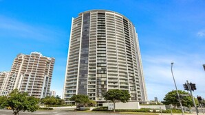 A high-rise building with a curved facade, multiple balconies, and a modern architectural design. - Hinterland Views 2BR apartment - Sierra Grand - CoastHM (Broadbeach)