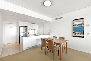 A modern kitchen with white cabinetry, a stainless steel refrigerator, and a dining area with a wooden table and chairs.
