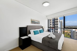 A modern hotel room with a large bed, a nightstand, a wall-mounted artwork, and a view of the city through large windows. - Hinterland Views 2BR apartment - Sierra Grand (Broadbeach)