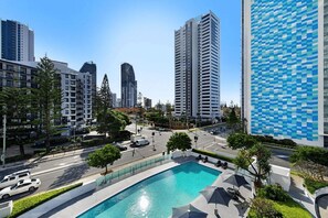 A modern urban setting with a swimming pool, high-rise buildings, and a clear sky. - Hinterland Views 2BR apartment - Sierra Grand (Broadbeach)